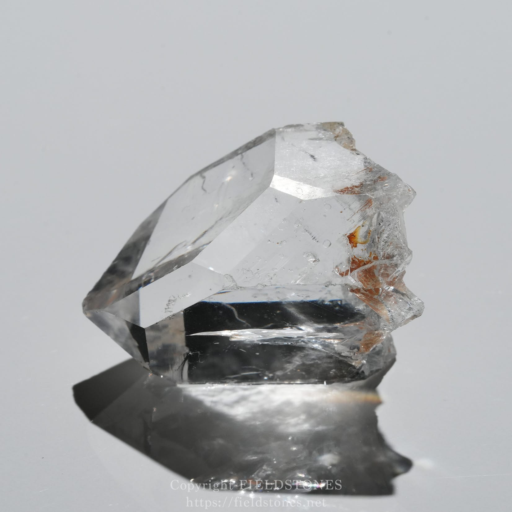 6571-1 - FieldStones Clear quartz crystal on a reflective surface, showing sharp facets and subtle inclusions in light.