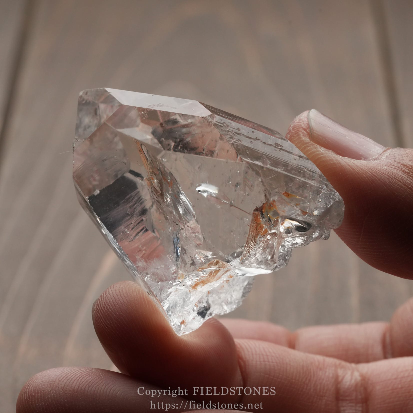 6571-10 - FieldStones Clear quartz crystal held between two fingers.