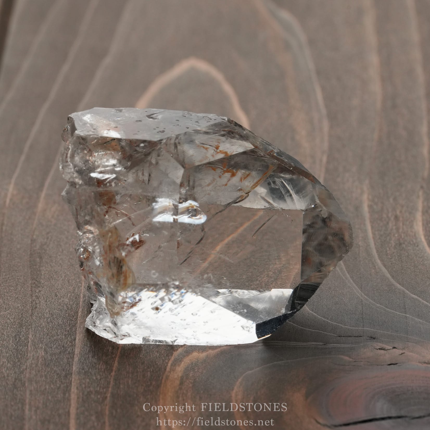 6571-16 - FieldStones Clear quartz crystal cluster on a dark wooden surface, showing translucent facets and natural imperfections.