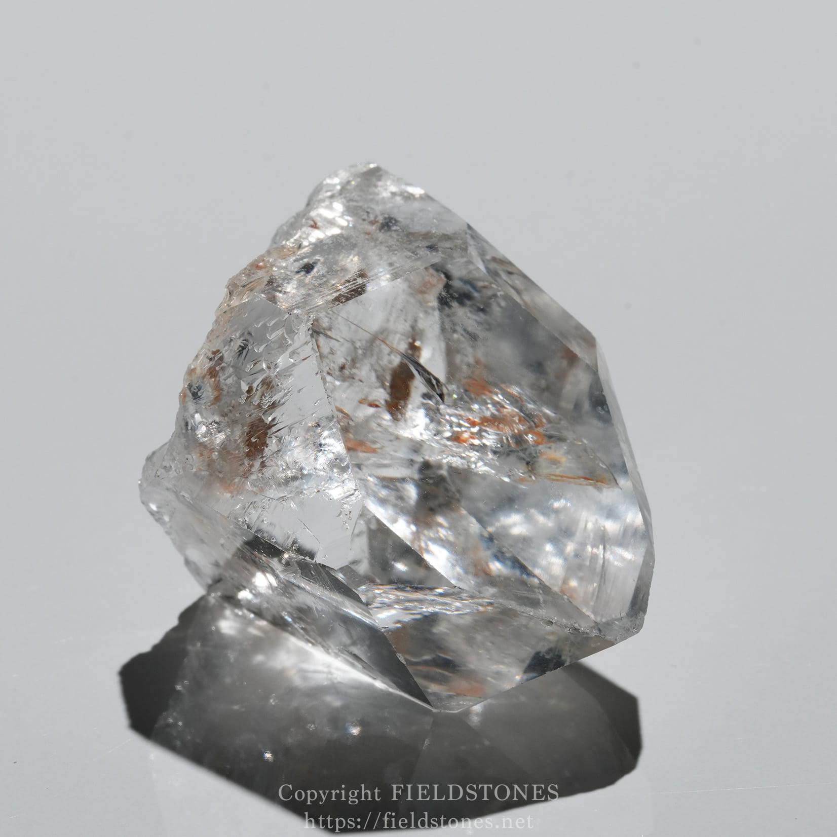 6571-4 - FieldStones Close-up of a clear quartz crystal with sharp, angular facets on a pale background.