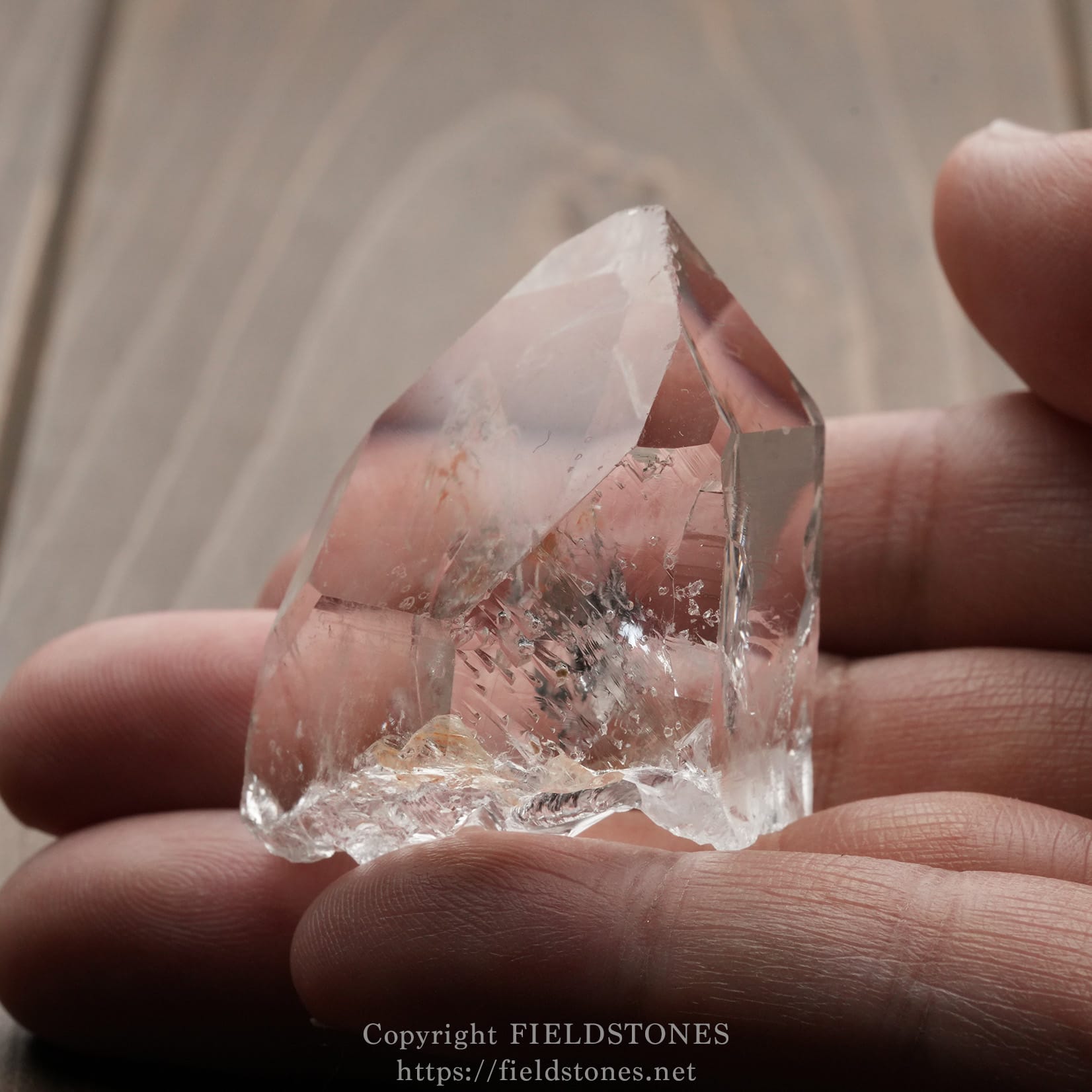 6571-8 - FieldStones Close-up of a pink-tinged quartz crystal held between two fingers.