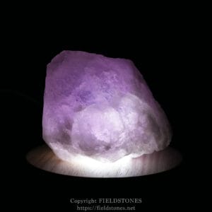 Rough pink amethyst crystal illuminated from below against a black background on a wooden surface.