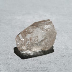 Close-up of a rough, translucent quartz crystal on a light gray textured surface.