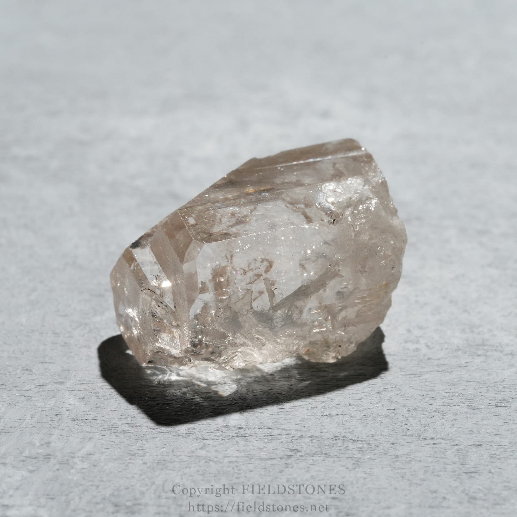 6576-1 - FieldStones Close-up of a rough, translucent quartz crystal on a light gray textured surface.