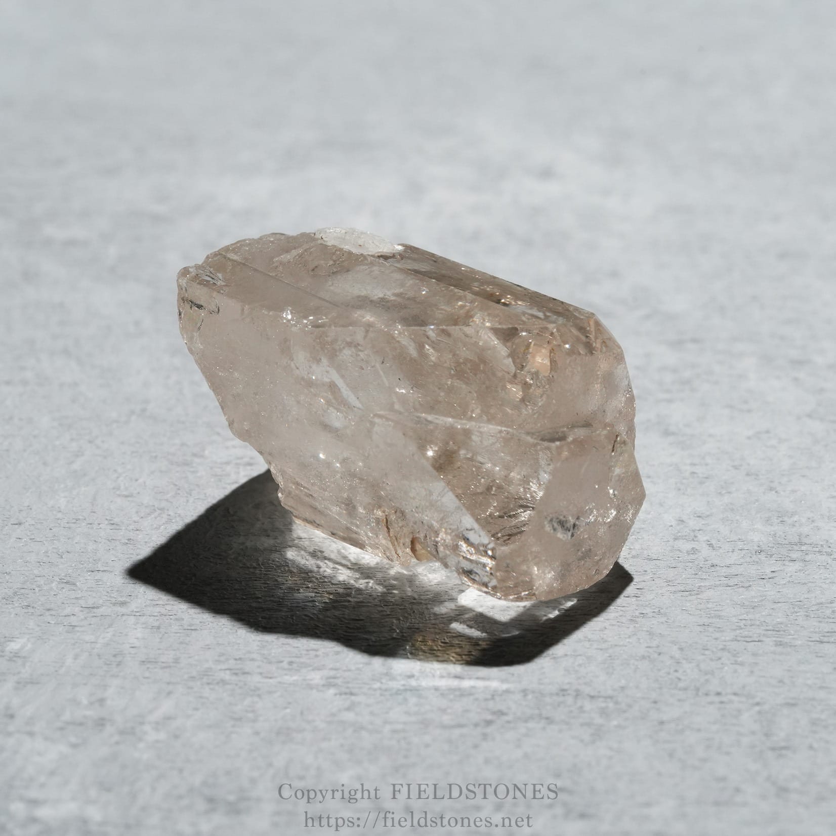 6576-6 - FieldStones Raw pink quartz crystal resting on a light gray surface