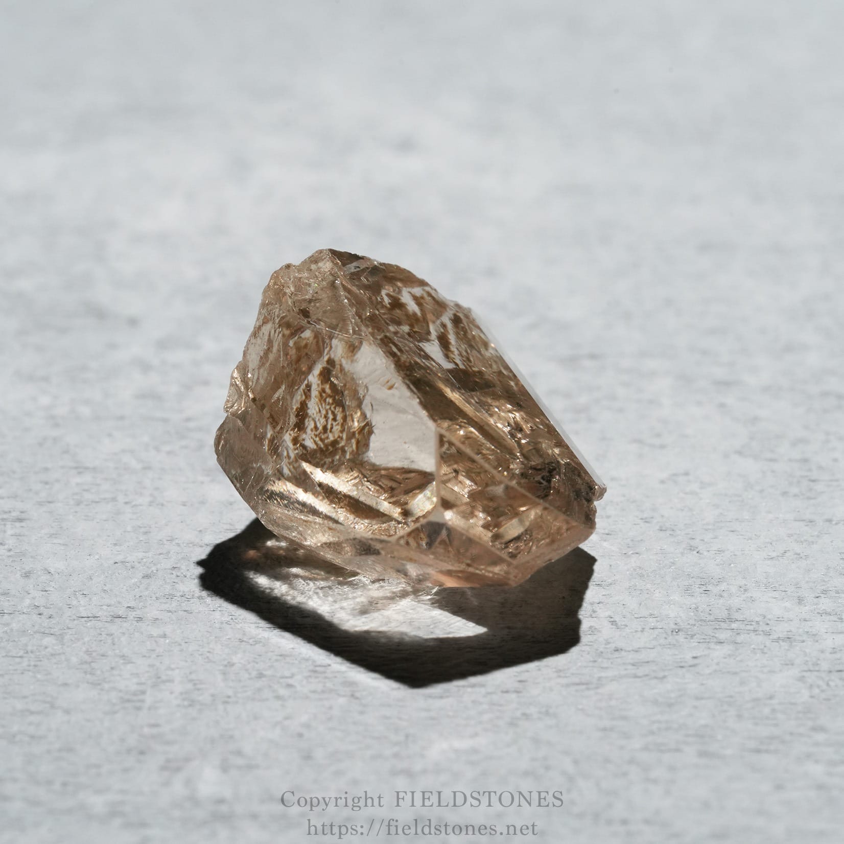 6578-2 - FieldStones Pink rose quartz crystal resting on a light gray, textured surface with a distinct shadow beneath it.