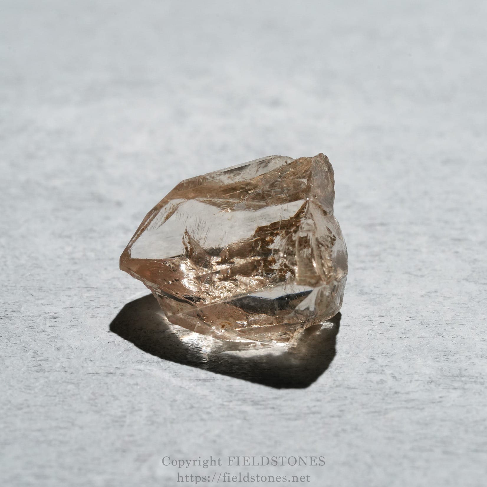 6578-4 - FieldStones Pink translucent quartz crystal resting on a gray textured surface, showing rough facets and a dark shadow beneath.