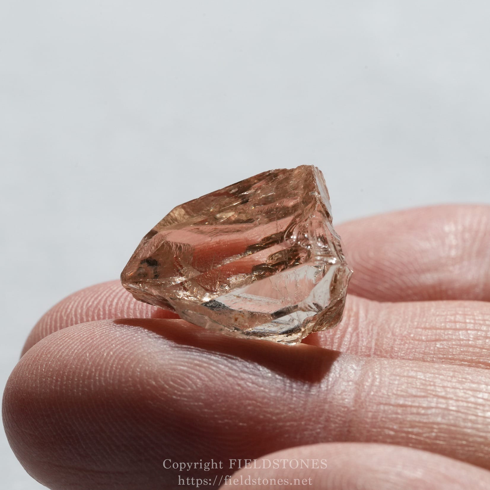 6578-7 - FieldStones Close-up of a jagged pink rose quartz crystal held between fingertips.