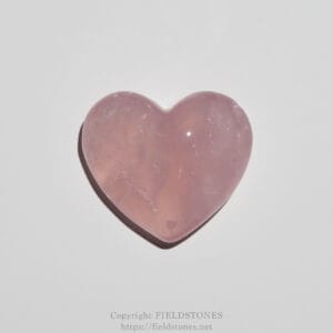 Polished pink heart-shaped rose quartz stone on a white surface.