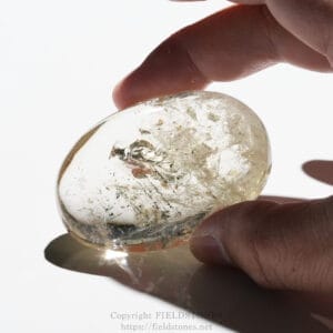 Close-up of a hand holding a polished, clear crystal with visible internal fractures against a white background.