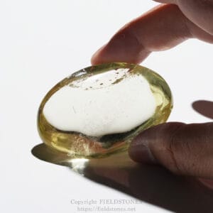 Close-up of a hand pinching a smooth, translucent yellow-green gemstone against a white background