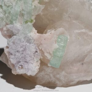 Close-up of a pink quartz matrix with pale green aquamarine crystals embedded, showing translucent, tabular crystals.