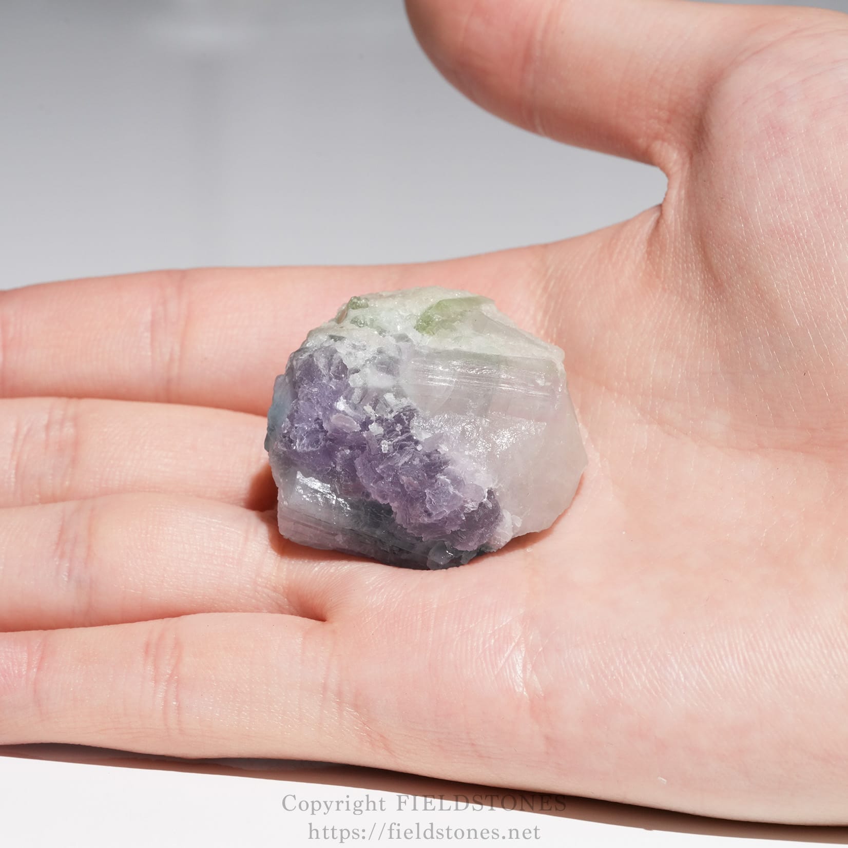 6645-10 - FieldStones Small rough crystal cluster with purple, green, and clear sections held in a person's fingers.