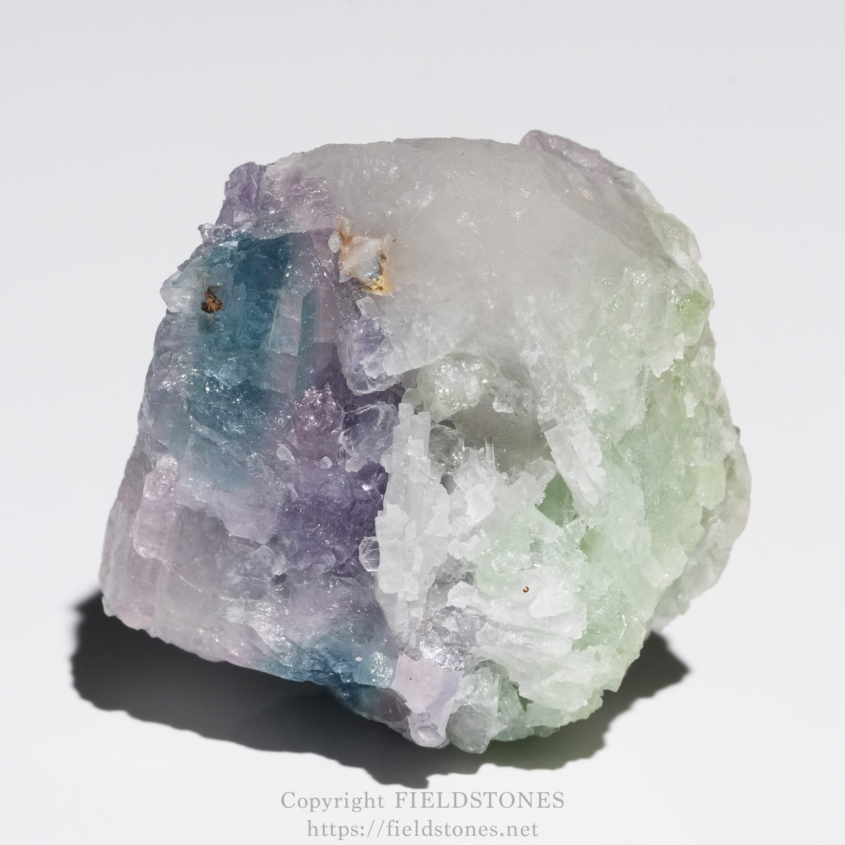 6645-8 - FieldStones Multicolored mineral crystal cluster (fluorite) with purple, blue, and green hues and rough, translucent facets against a white background.