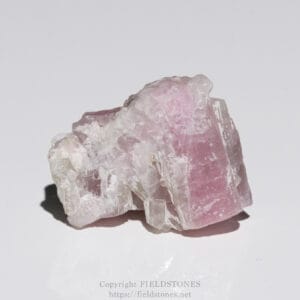 Pink rose quartz crystal cluster resting on a white surface, showing translucent pink facets and rough edges.