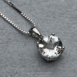 Close-up of a silver chain necklace with a large, round, faceted clear gemstone pendant on a gray background.