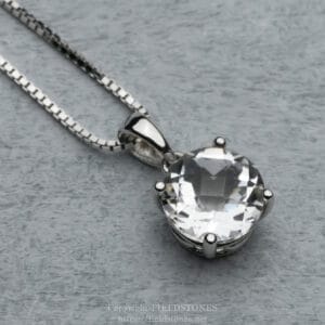 Silver necklace with a large faceted clear gemstone pendant on a grey background.