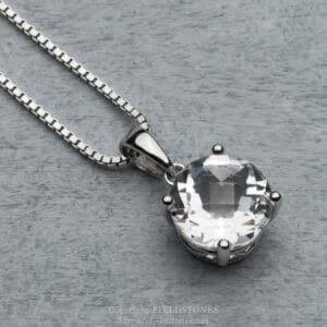 Silver chain necklace with a large clear faceted pendant resting on a gray wooden surface