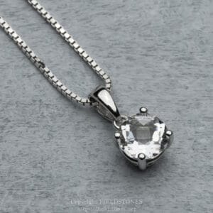Silver chain necklace with a large round-cut clear gemstone pendant set in a silver bezel against a gray textured background.