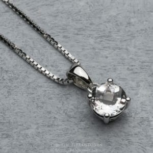 Silver necklace with a large faceted crystal pendant resting on a grey surface.