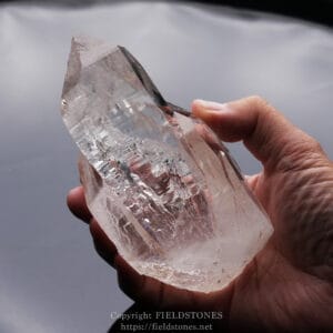Close-up of a hand holding a large transparent quartz crystal.