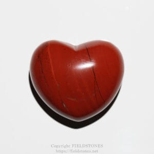 Glossy red heart-shaped stone with dark veins against a white background.