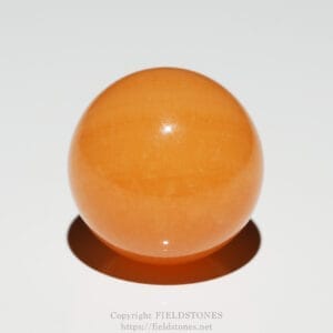 Close-up of a glossy orange sphere resting on a white surface with a soft shadow beneath it