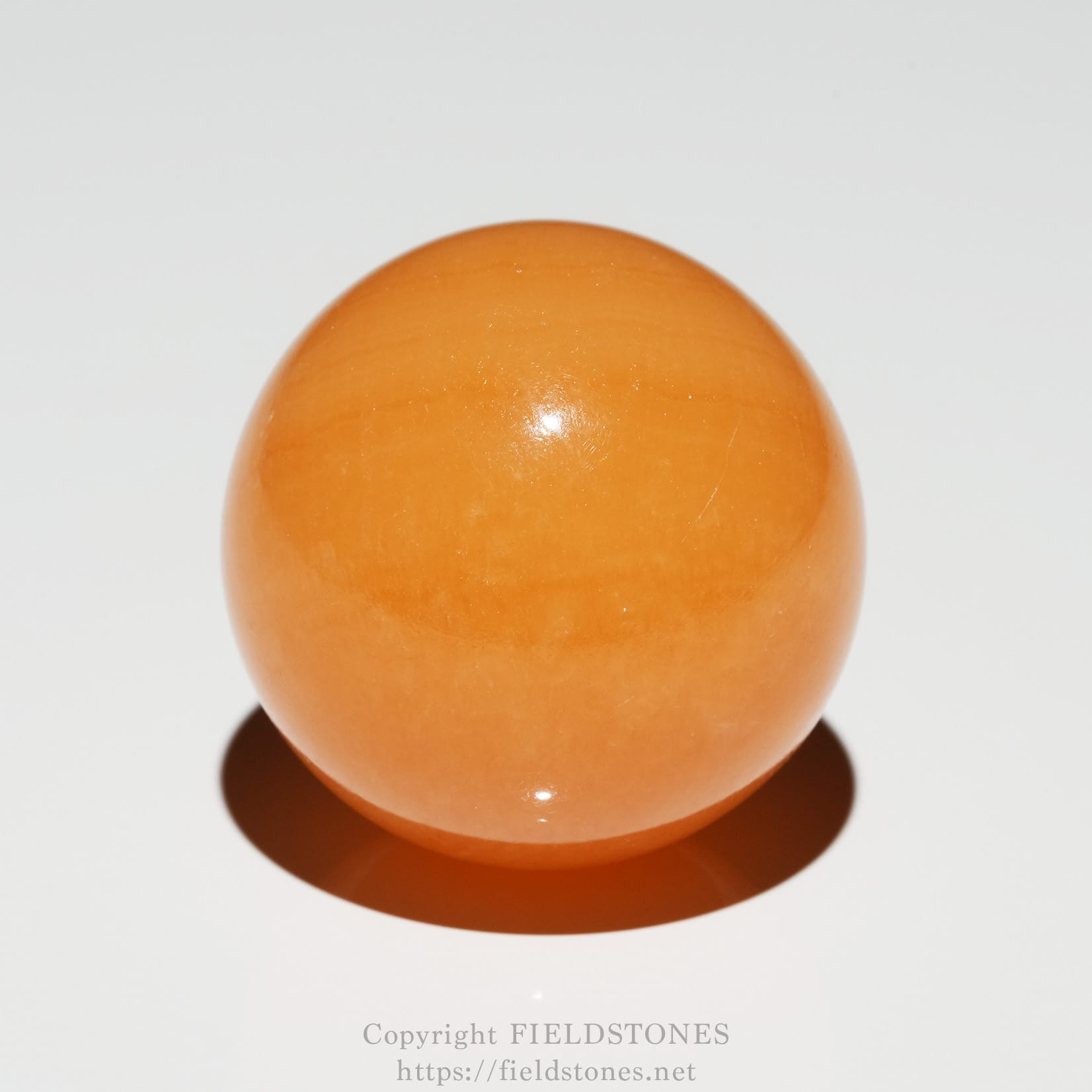6676-1 - FieldStones Close-up of a glossy orange sphere resting on a white surface with a soft shadow beneath it
