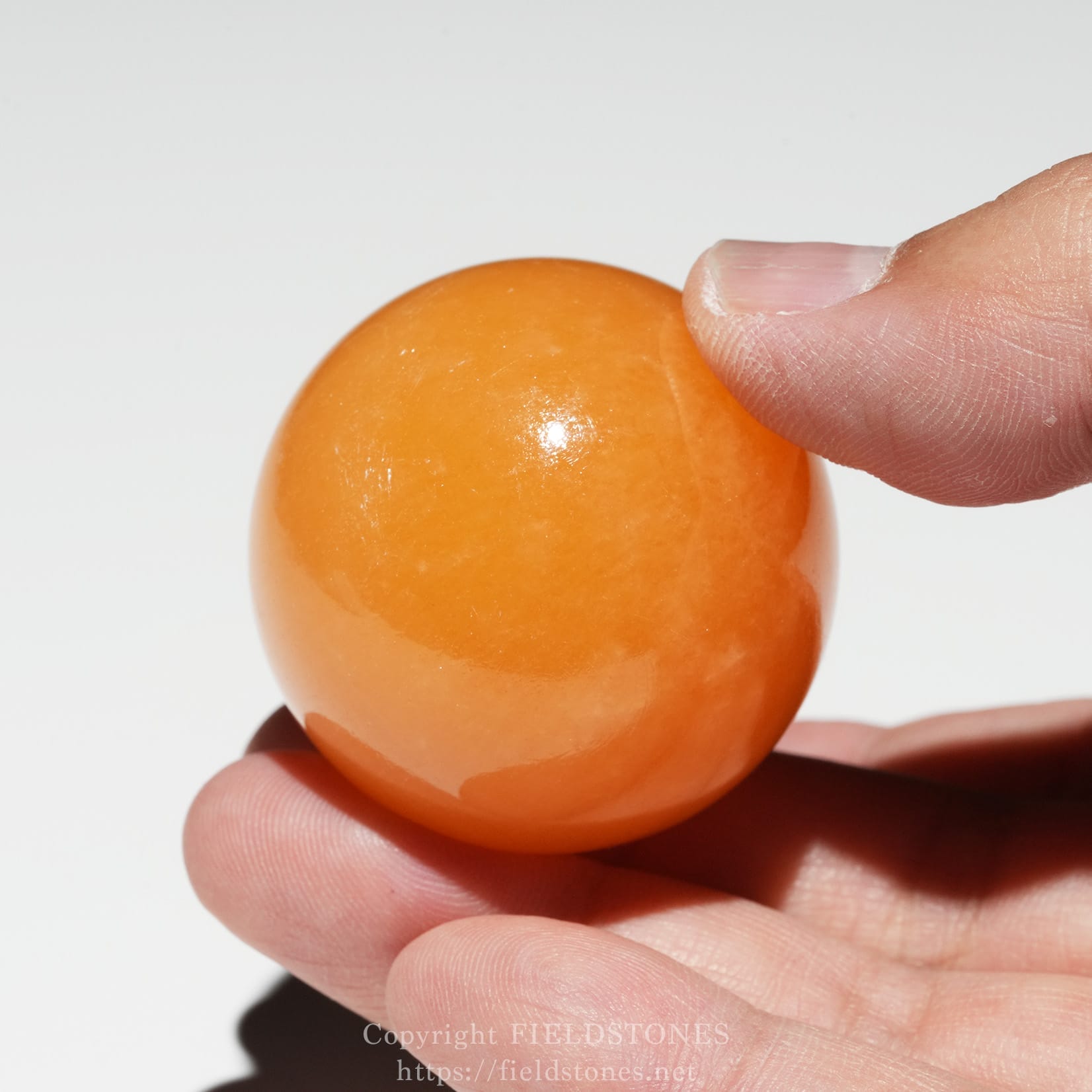 6676-6 - FieldStones Close-up of a fingertip pinching an orange glossy ball, likely a small rubber or plastic ball handle-thumb grip model.