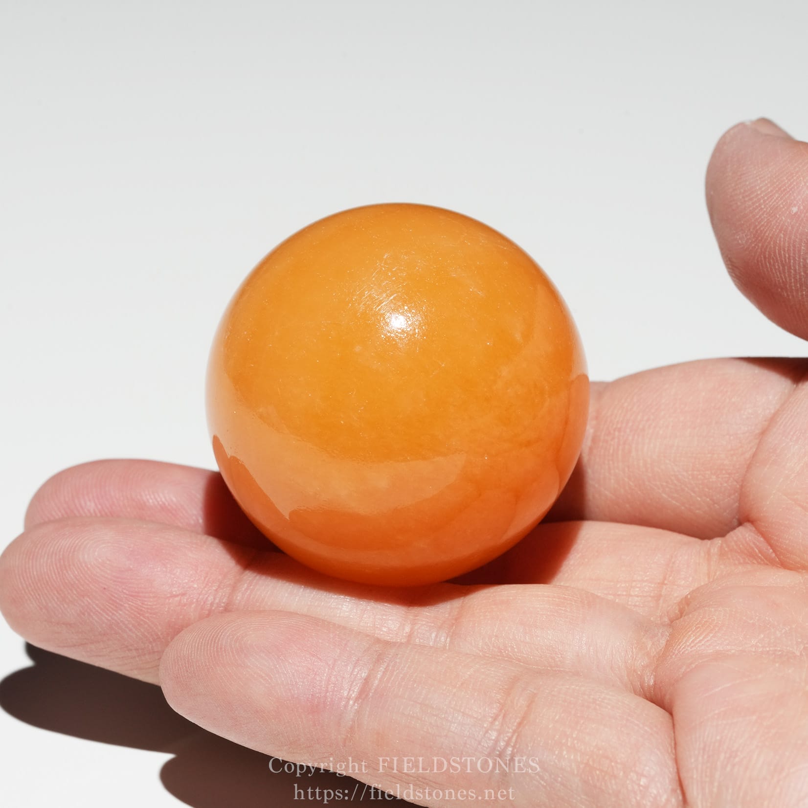 6676-7 - FieldStones Glossy orange ball held between two fingers against a white background.