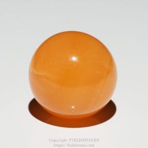 Glossy orange sphere on a white surface casting a shadow below.