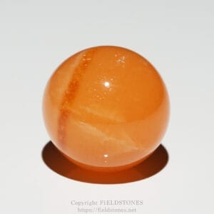 Close-up of an orange marble with white marbling, resting on a white surface and casting a shadow