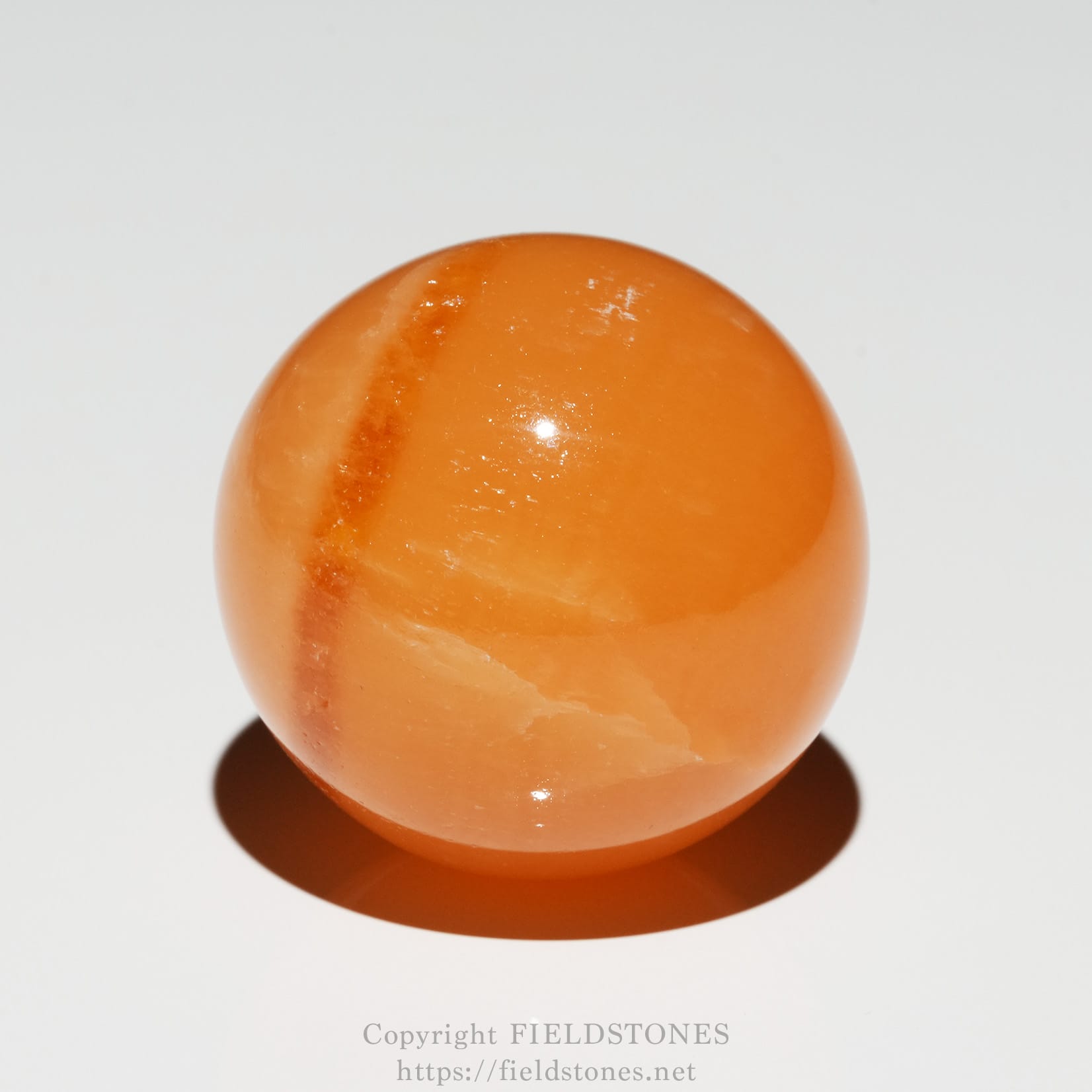 6678-1 - FieldStones Close-up of an orange marble with white marbling, resting on a white surface and casting a shadow