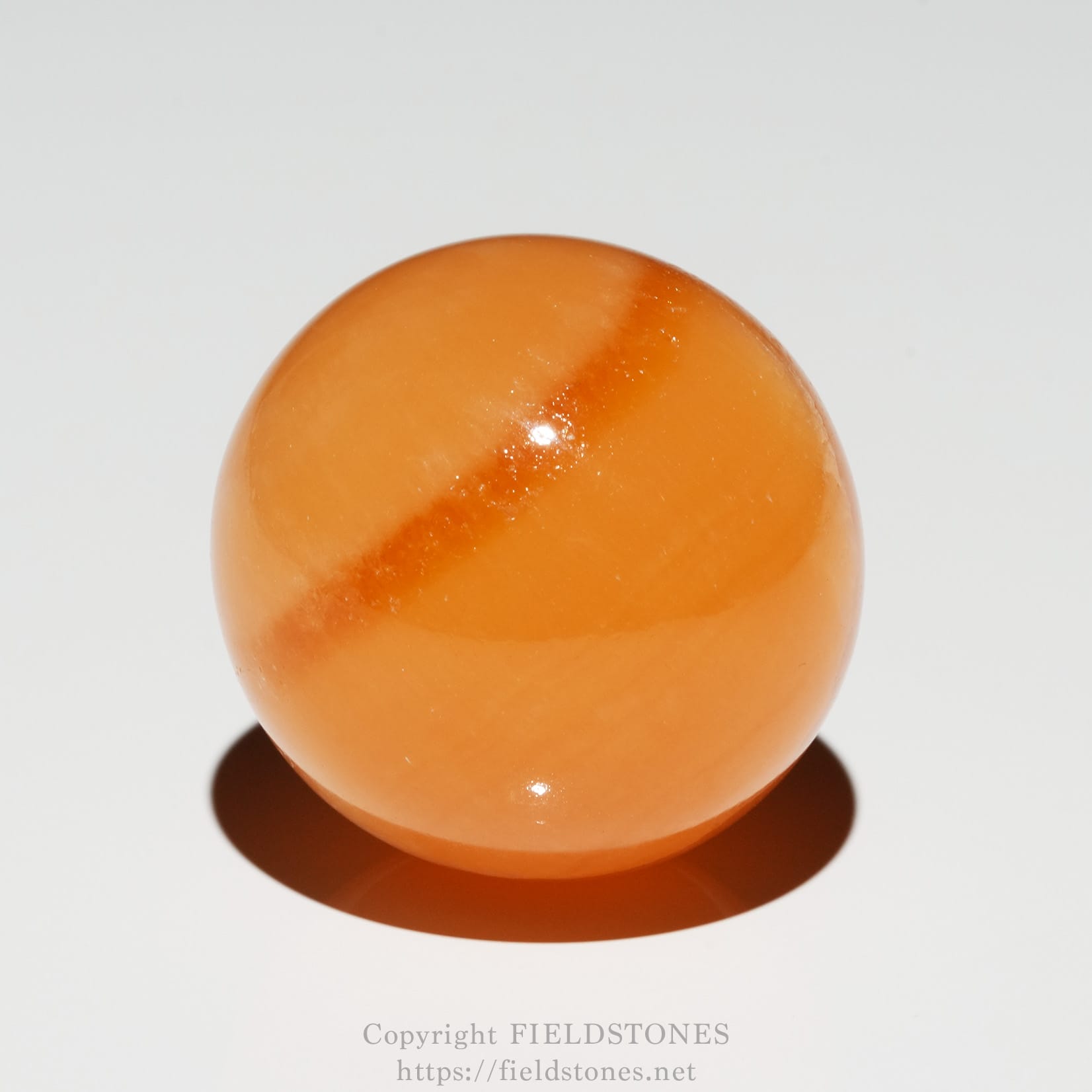 6678-2 - FieldStones Glossy orange sphere on a white background with a soft shadow underneath into the bottom edge of the frame.