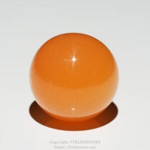 Close-up of an orange, glossy sphere resting on a white surface with a soft shadow below.