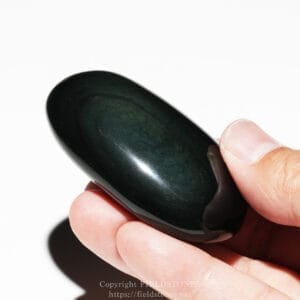 Close-up of a smooth, dark green-black polished stone bead held between a thumb and index finger against a light background