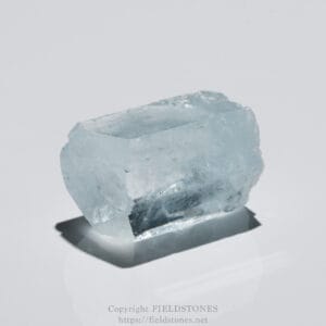 Pale blue crystal block with sharp facets resting on a white surface.