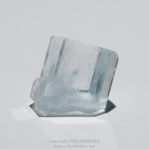 Close-up of a rectangular aquamarine crystal tilted on a white background, showing its pale blue facets and edges.