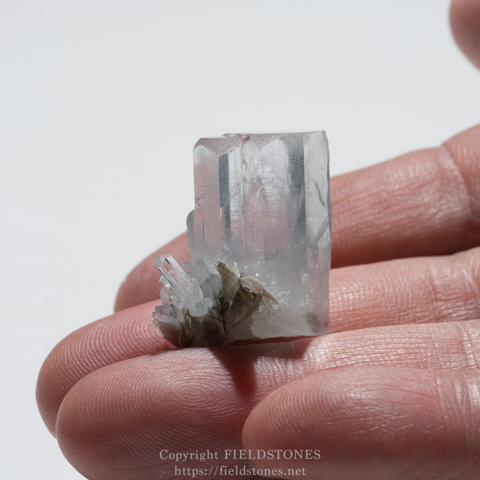 6690-10 - FieldStones Clear quartz crystal cluster held between fingers, showing sharp prism faces and a small secondary cluster at the base.