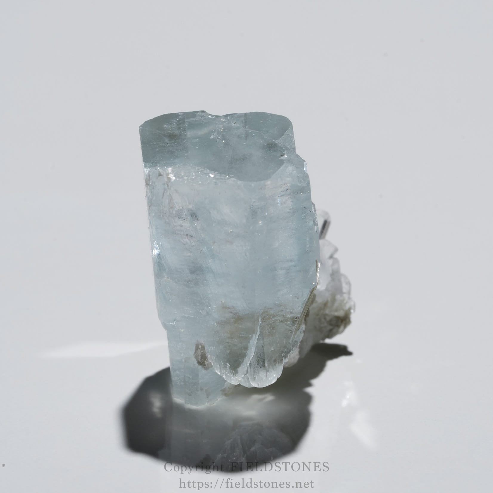6690-5 - FieldStones Light blue aquamarine crystal with a pointed termination perched on a white surface.