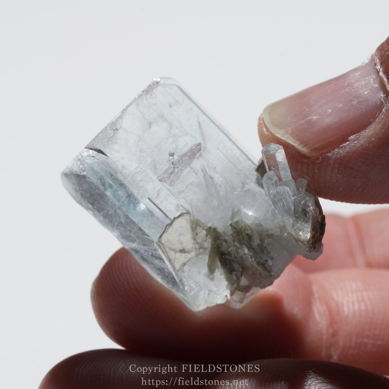6690-7 - FieldStones Close-up of a translucent quartz crystal held between fingers, showing jagged facets and cloudy inclusions.