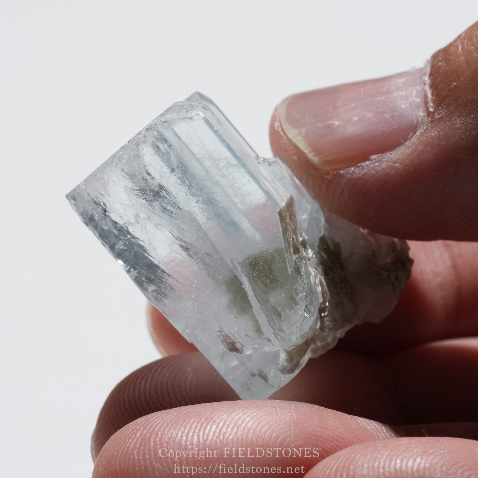 6690-9 - FieldStones Close-up of a clear quartz crystal between fingertips, showing its transparent, faceted edges.