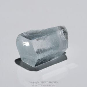 Close-up of a pale blue-gray quartz crystal with sharp, faceted faces on a white surface.