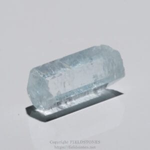 Close-up of a pale blue hexagonal crystal on a white surface.