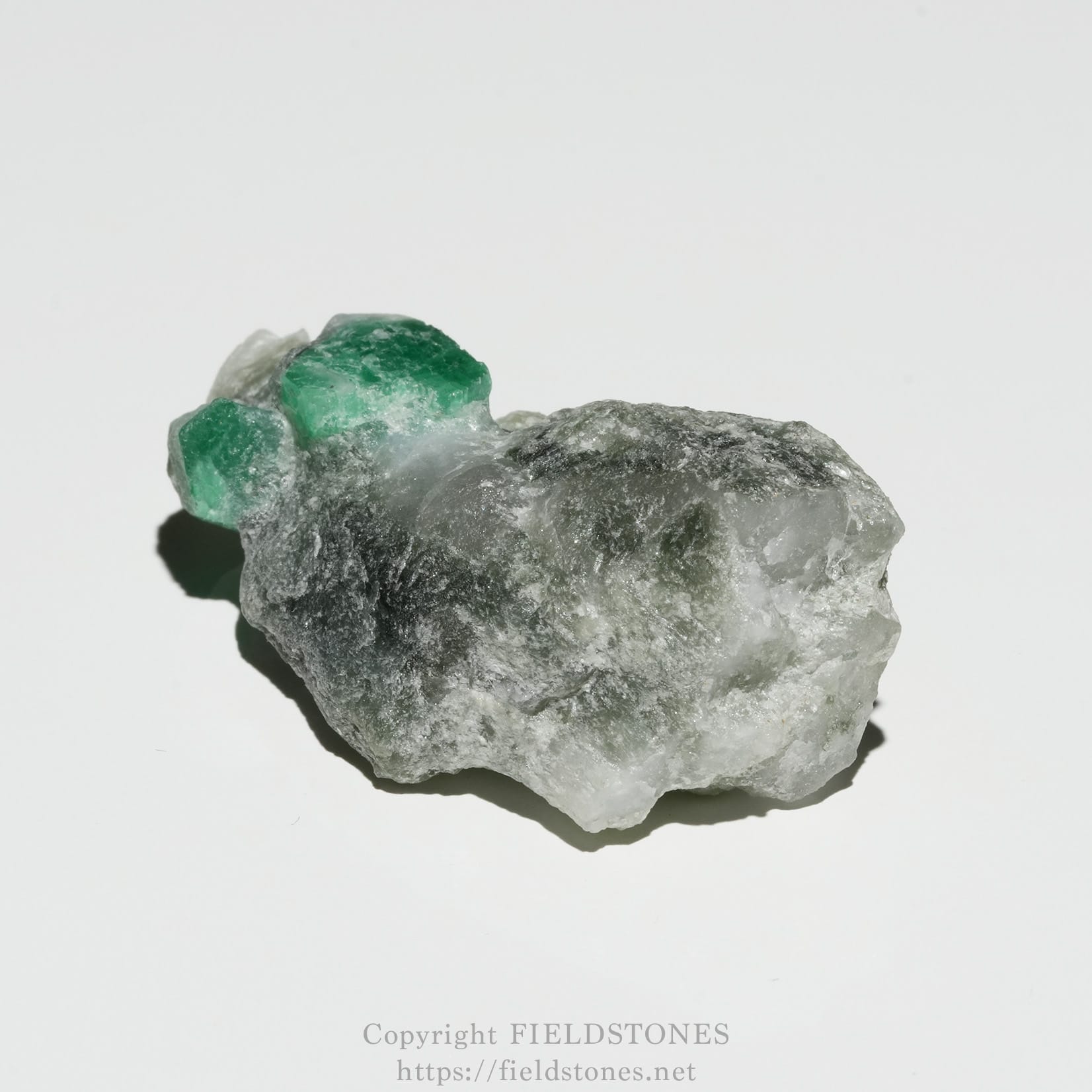 6696-3 - FieldStones Rough gray rock with a cluster of bright emerald-green crystals on top photographed against a pale background.