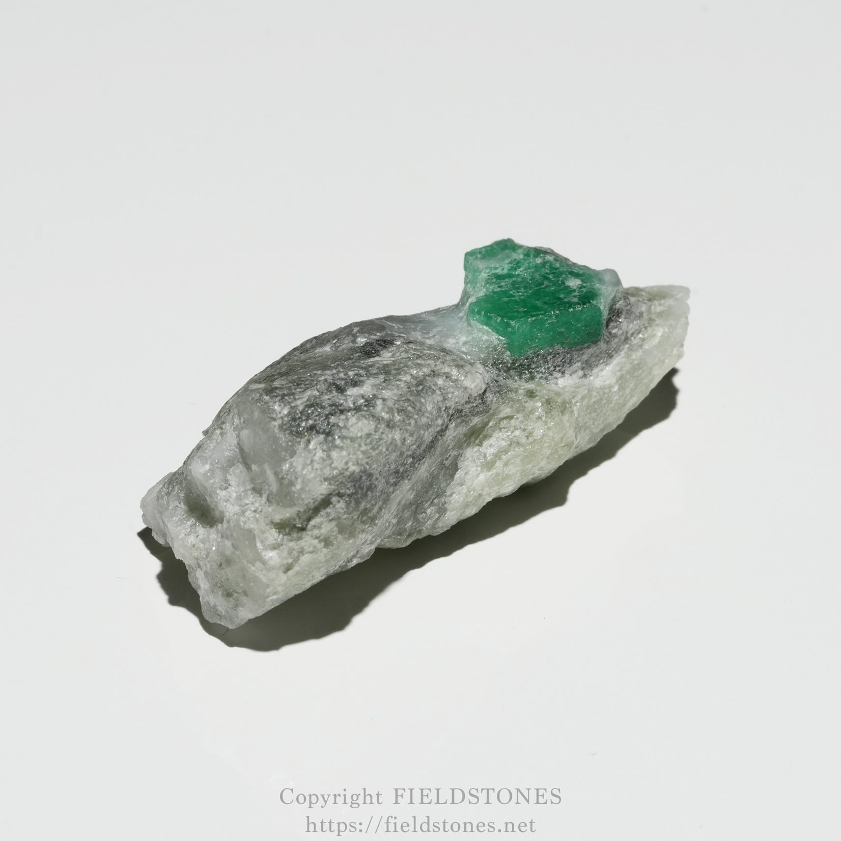 6696-4 - FieldStones Small green mineral crystal perched on a rough gray-white rock specimen surface.