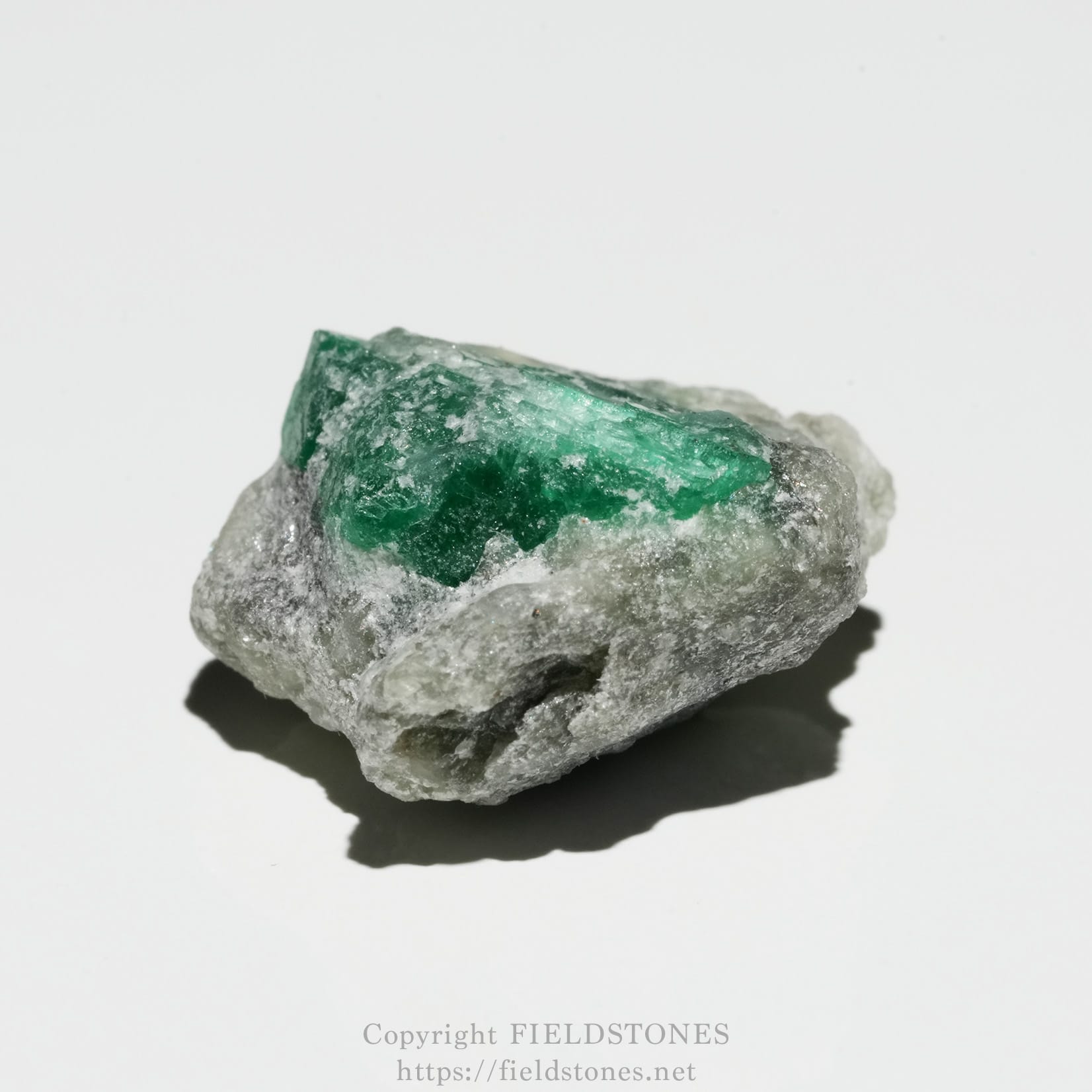 6700-3 - FieldStones Rough emerald crystal embedded in gray rocky matrix on a white background