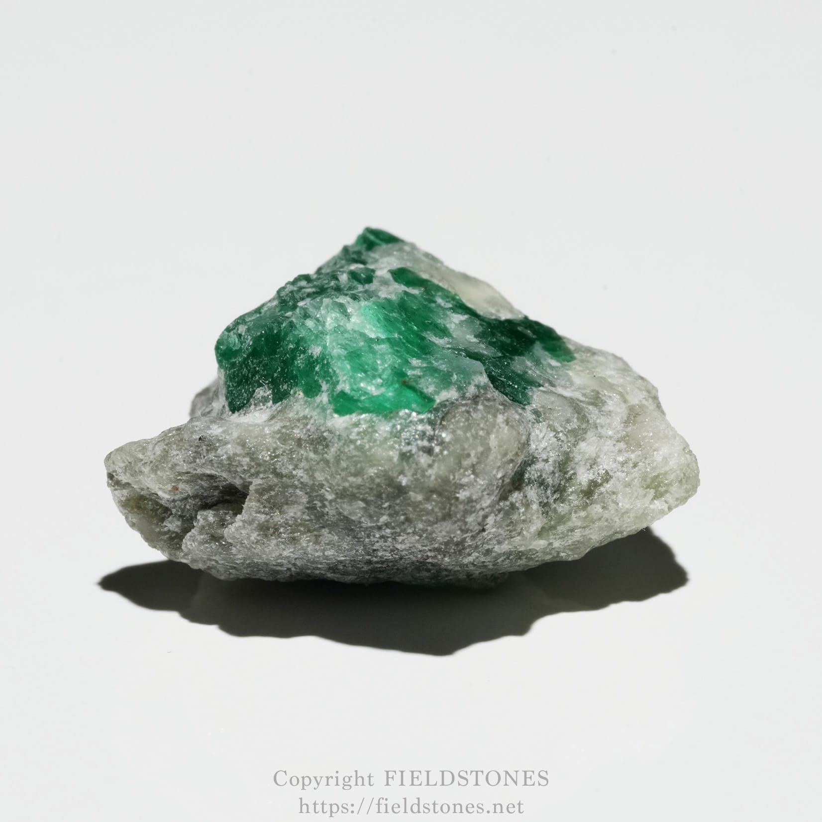 6700-4 - FieldStones Rough gray rock with bright emerald-green crystals on top, set against a white background.