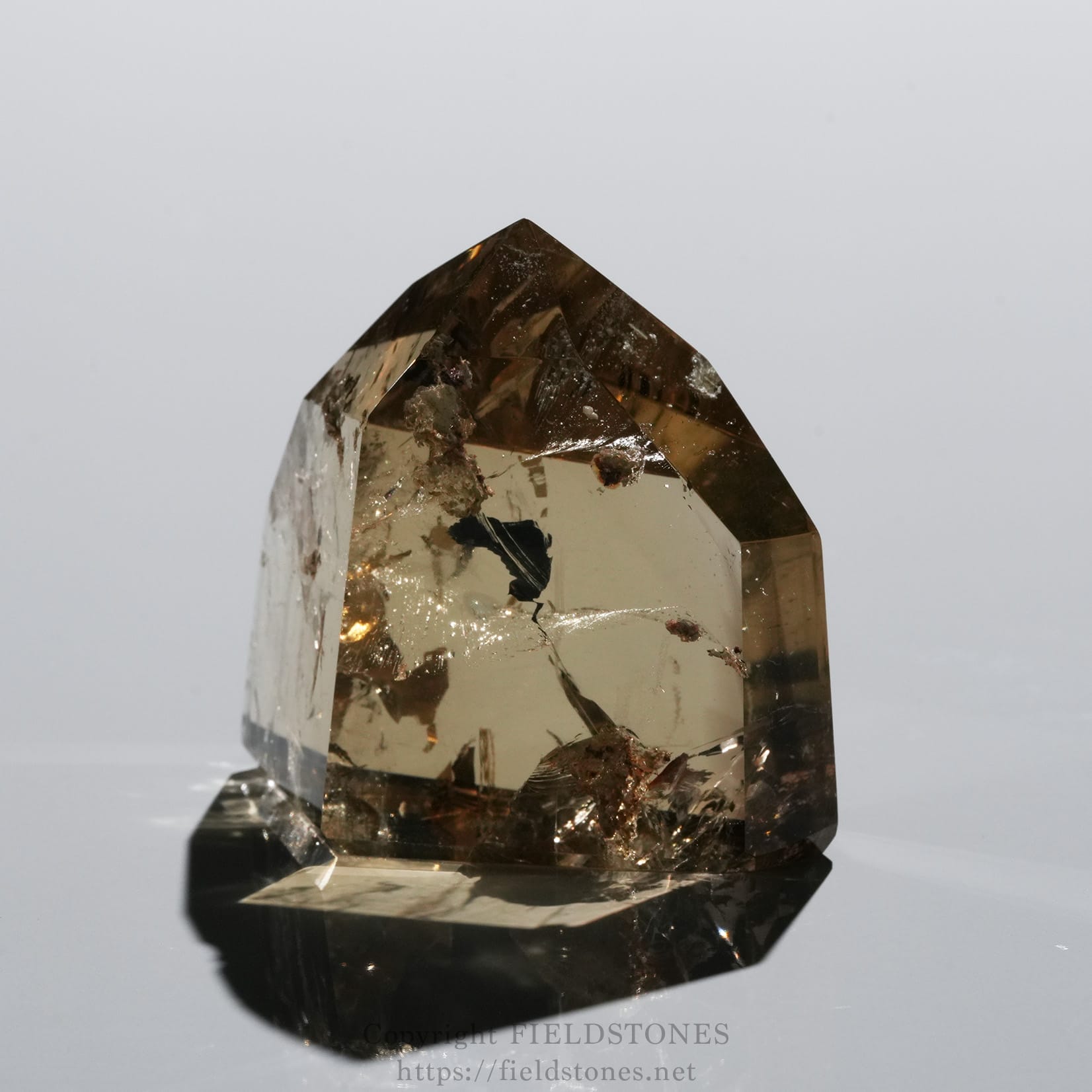 6708-5 - FieldStones Brown smoky quartz crystal point with rough inclusions on a reflective black base, photographed close-up.