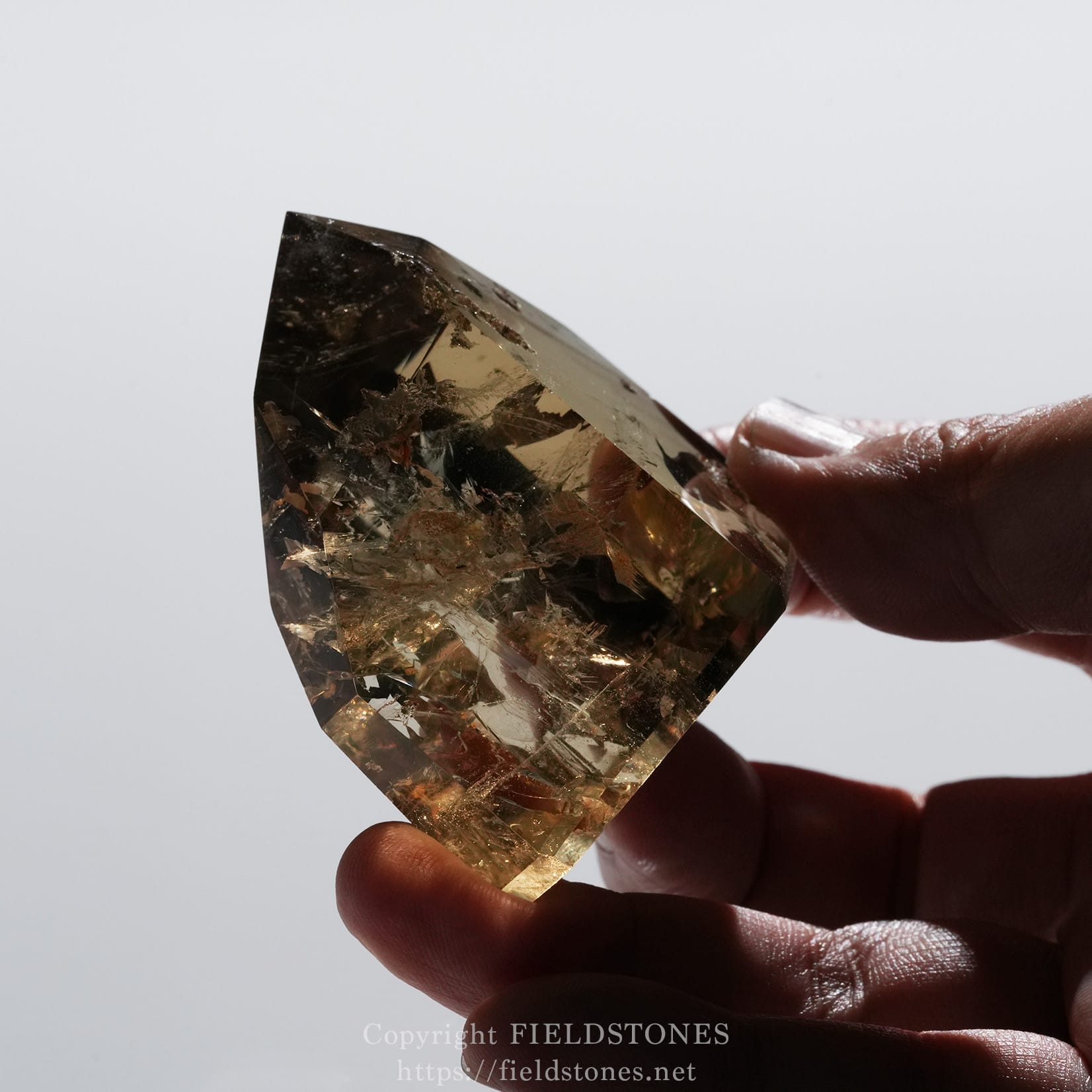 6708-9 - FieldStones Person holds a large faceted smoky quartz crystal between fingers against a light background, close-up view